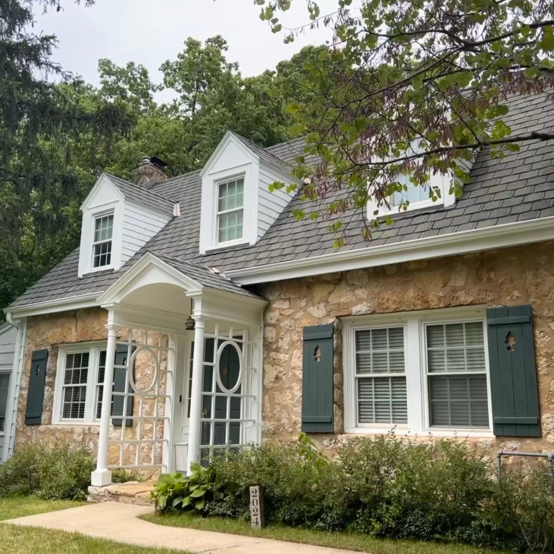 Exterior of a charming cottage-style home featuring a stone base, transformed by Painters Pro KC with green shutters and white trim to enhance its character.